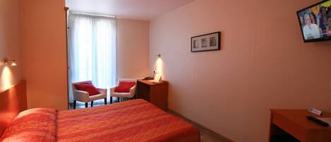 A hotel room with a large bed, a desk with a chair, a television, and a window with curtains.