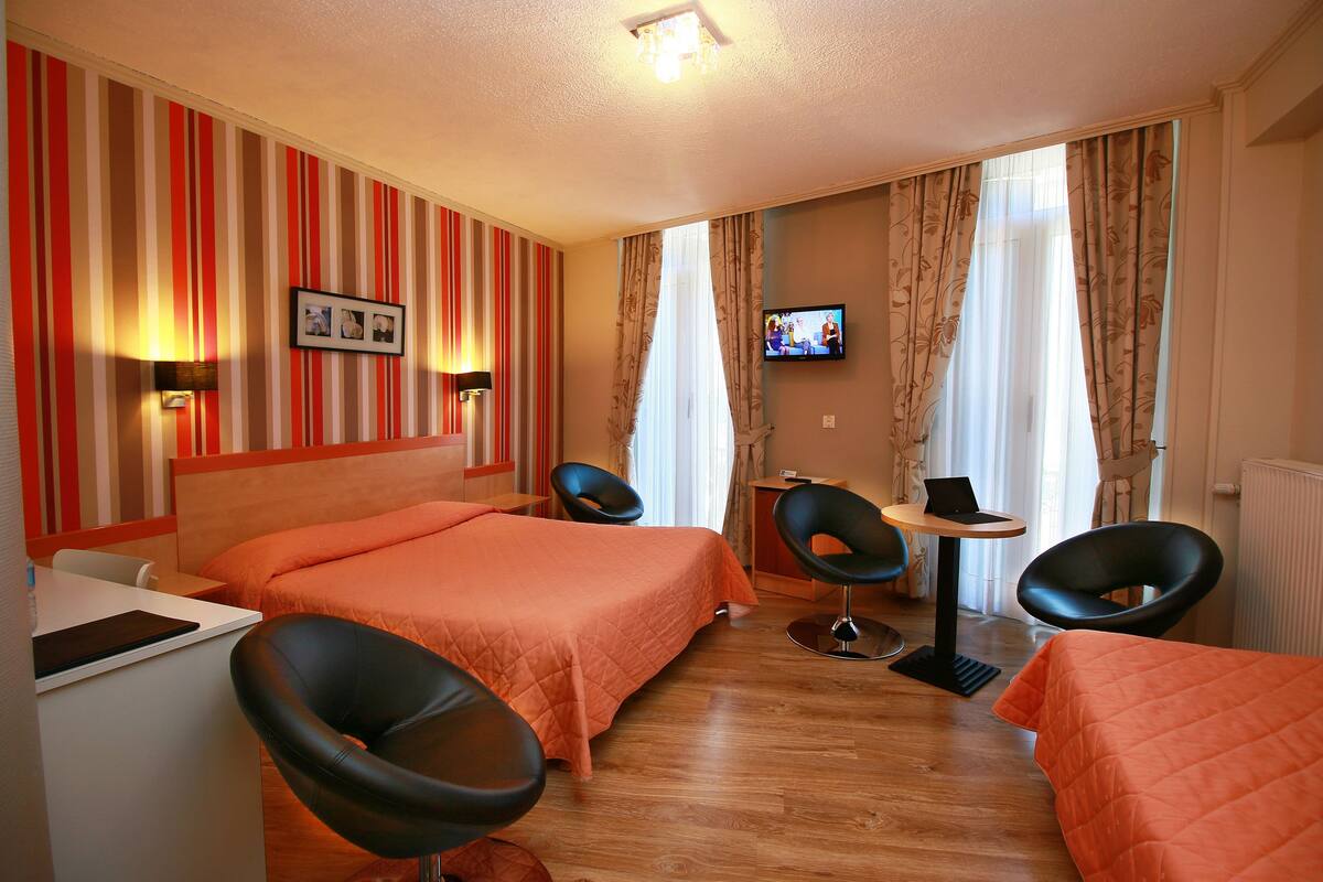 A hotel room with two beds, a desk, a chair, a TV, and curtains.
