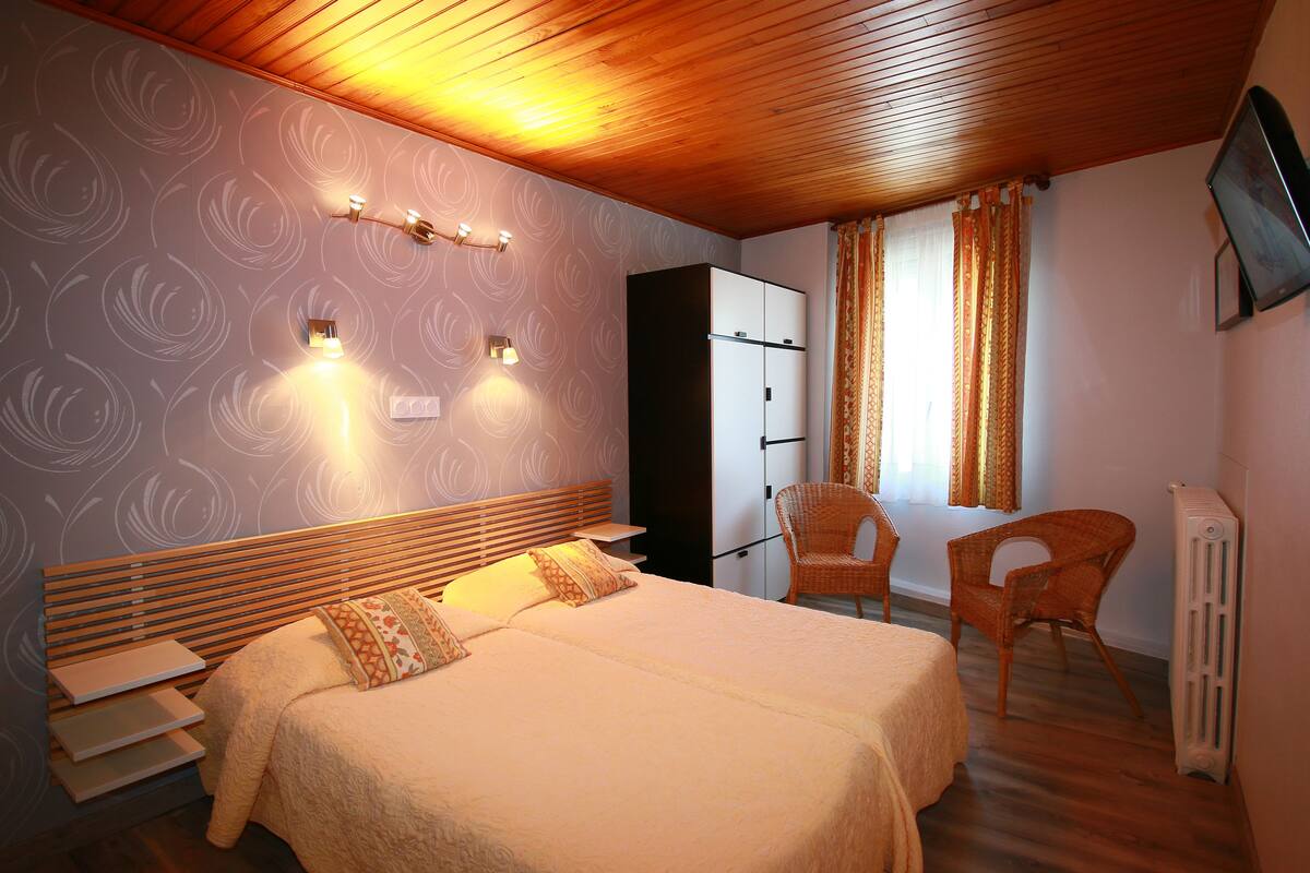 A hotel room with two beds, a wardrobe, a chair, and a television.