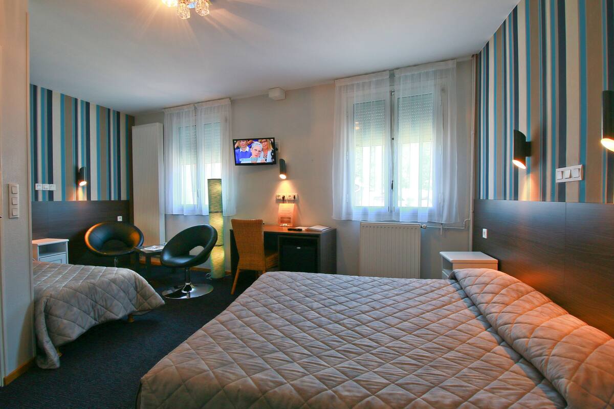 A hotel room with two beds, a desk, a chair, a television, and a window with curtains.