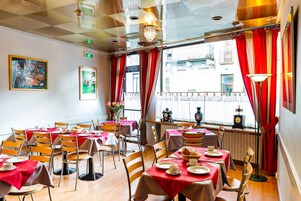 Zona pranzo con tavoli apparecchiati, sedie e un'ampia finestra con tende rosse.