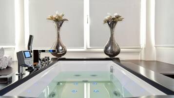 A modern bathroom with a glass-enclosed bathtub, two decorative vases with flowers, and a control panel with a digital display.