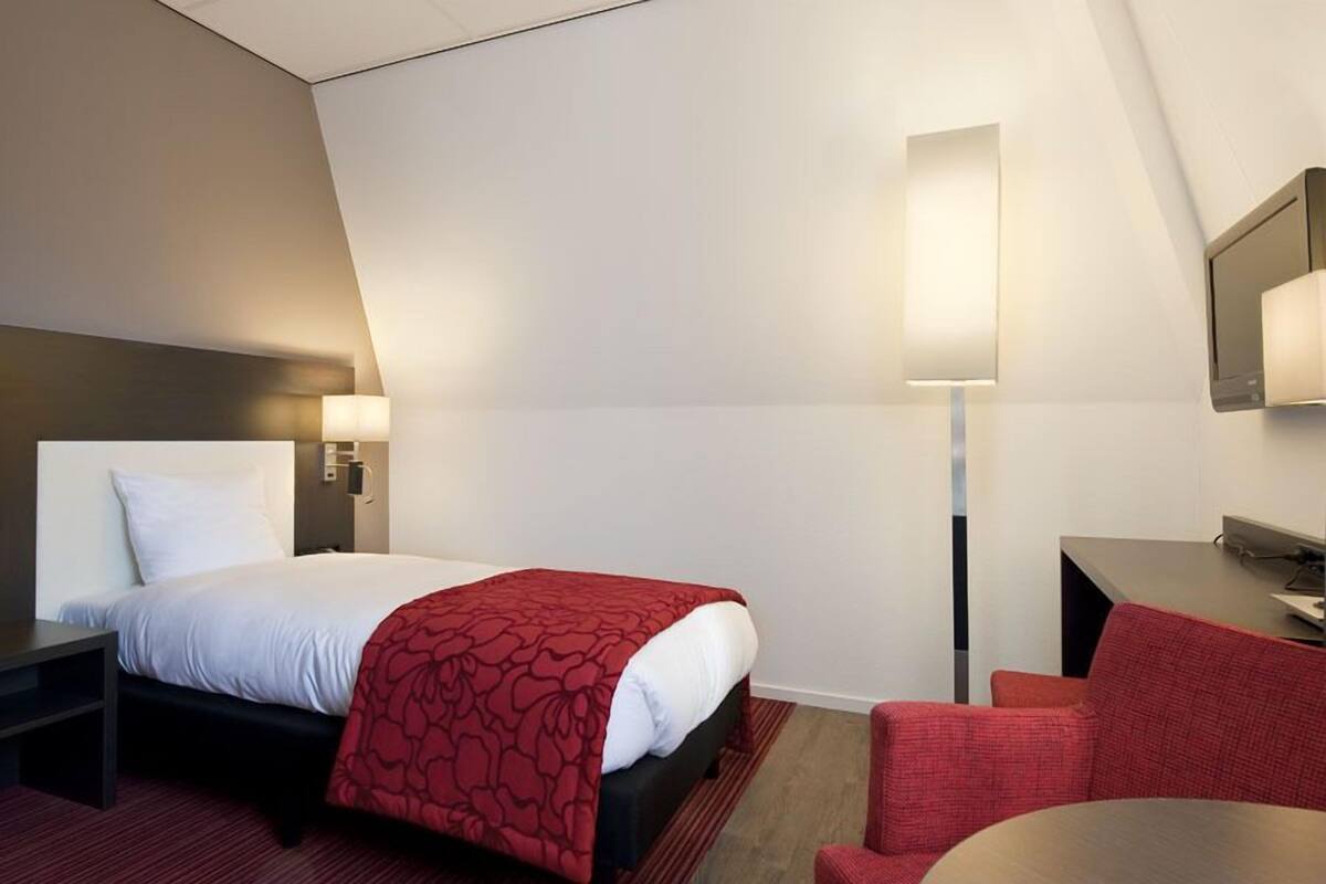 A hotel room with a bed, a desk, a chair, and a TV.