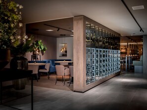 Un espace bar moderne avec un présentoir à vin, des sièges et une grande plante en pot.
