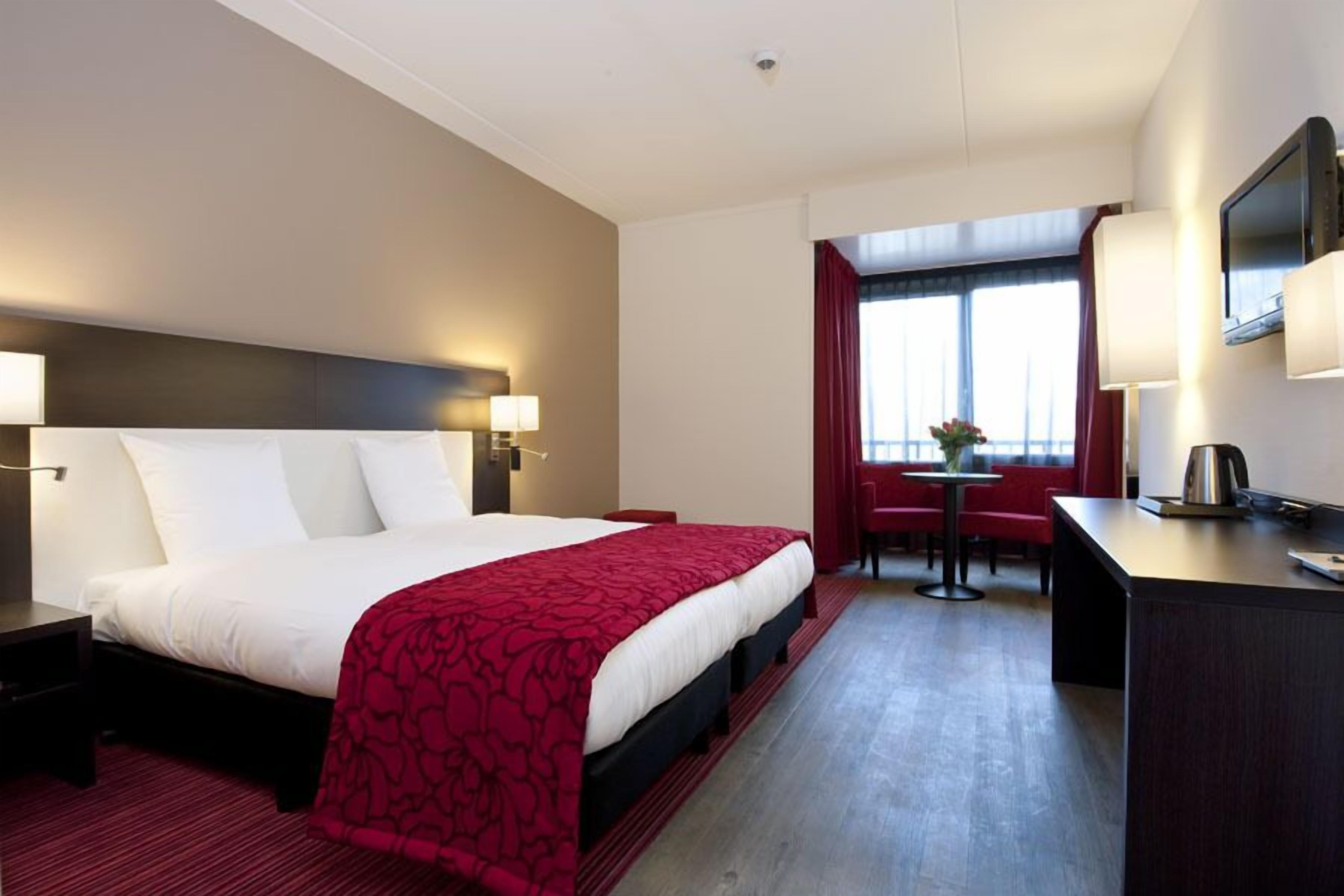 Hotelkamer met een groot bed, nachtkastjes, een bureau, een stoel, een televisie en een raam met gordijnen.