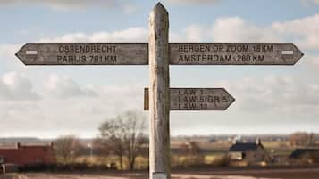 Un panneau indicateur en bois, avec des indications de direction et des distances vers Ossendrecht, Paris, Bergen op Zoom et Amsterdam.