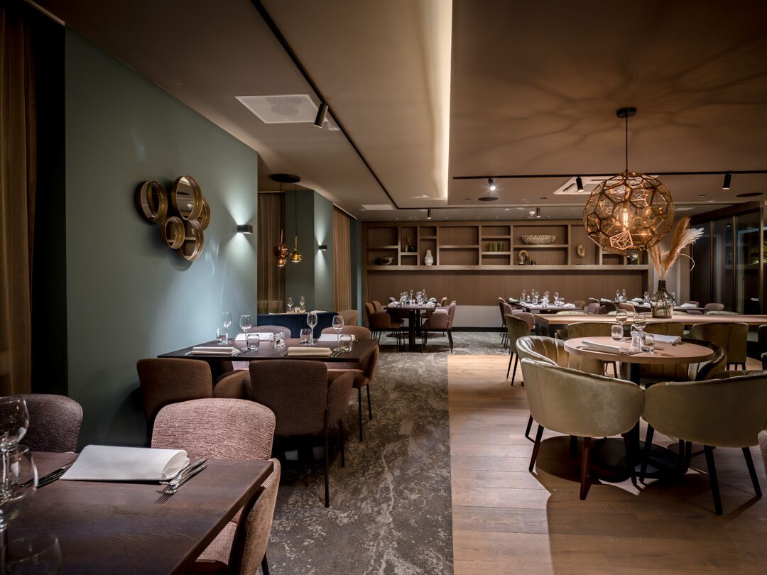 A modern dining area with multiple tables and chairs, a central light fixture, and a wall-mounted decorative piece.