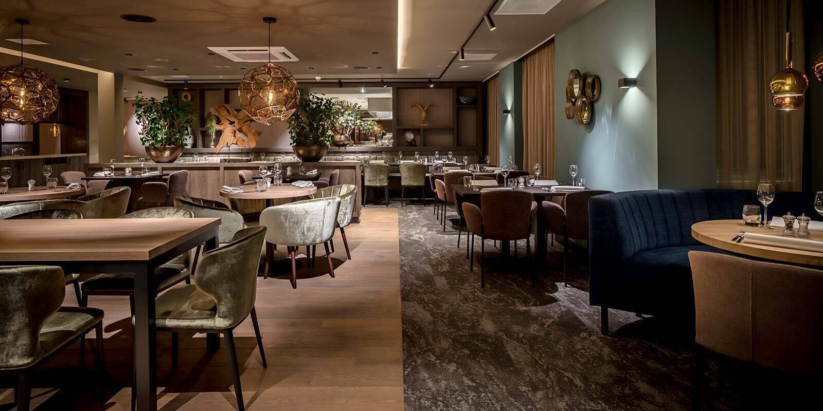 A modern restaurant interior with round tables, cushioned chairs, and a mix of pendant and wall lighting.