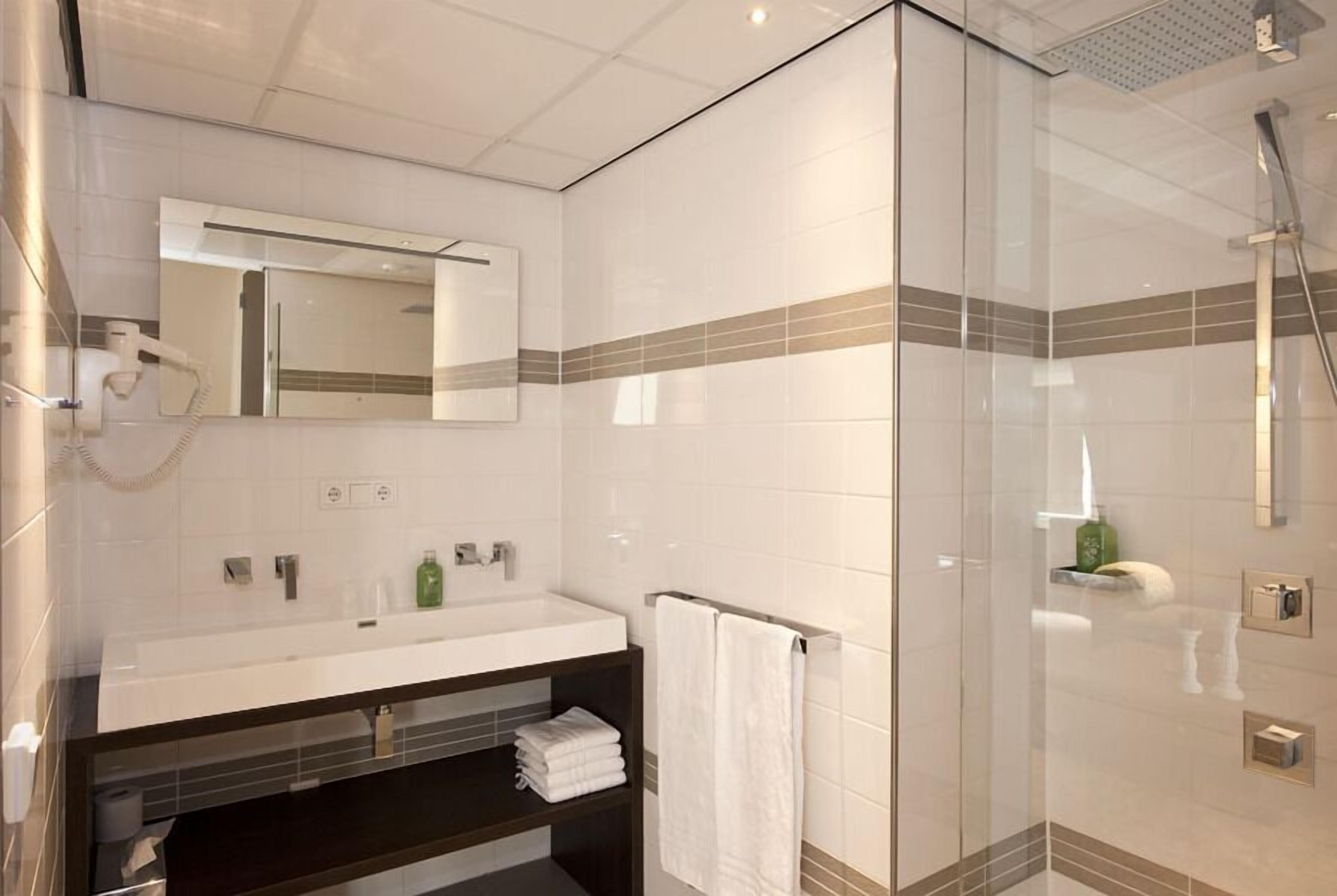 A modern bathroom with a glass shower enclosure, a large mirror, and a white sink with a dark countertop.