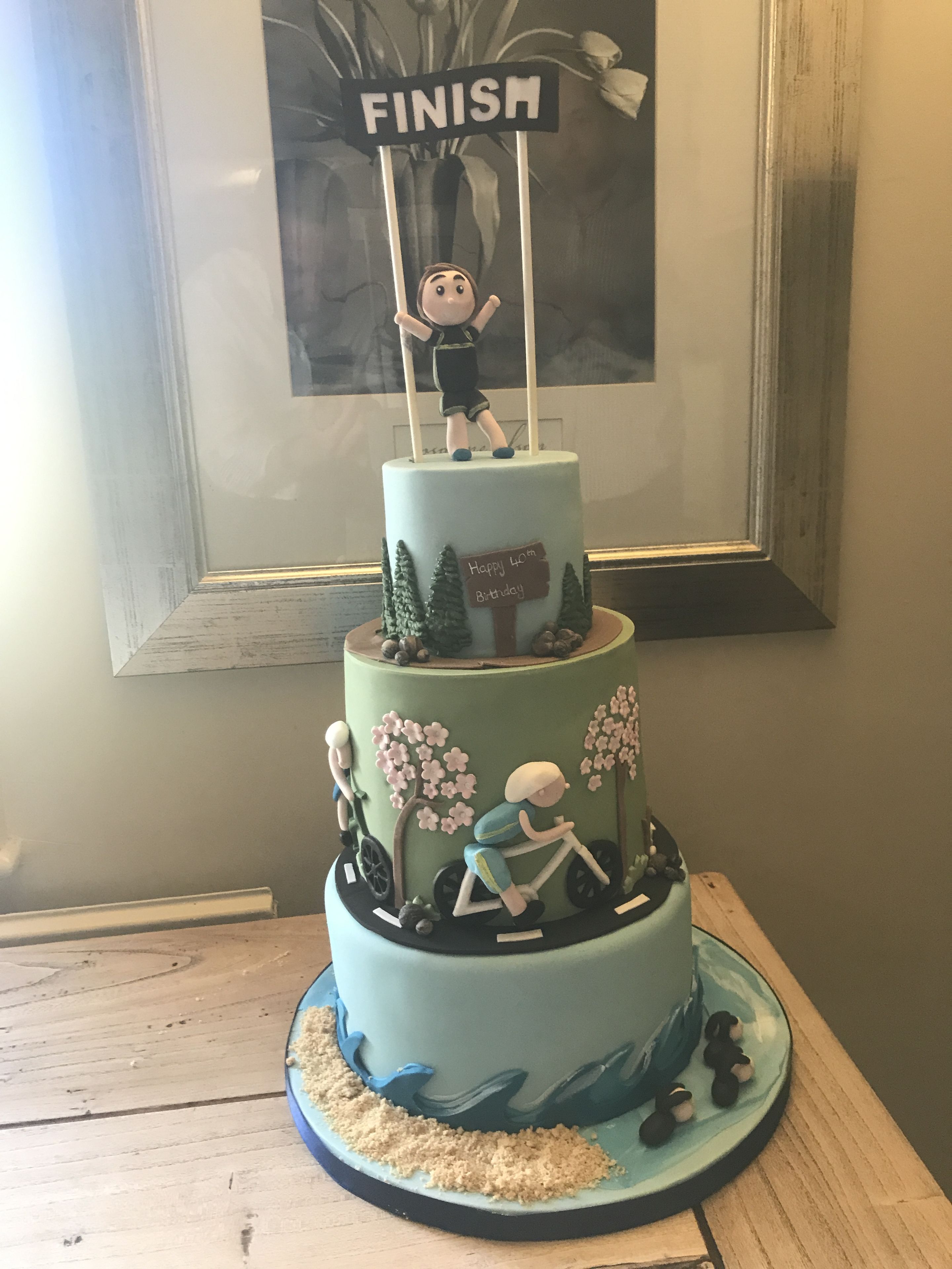 A multi-tiered cake with a 'Finish' sign on top, decorated with figures and trees.