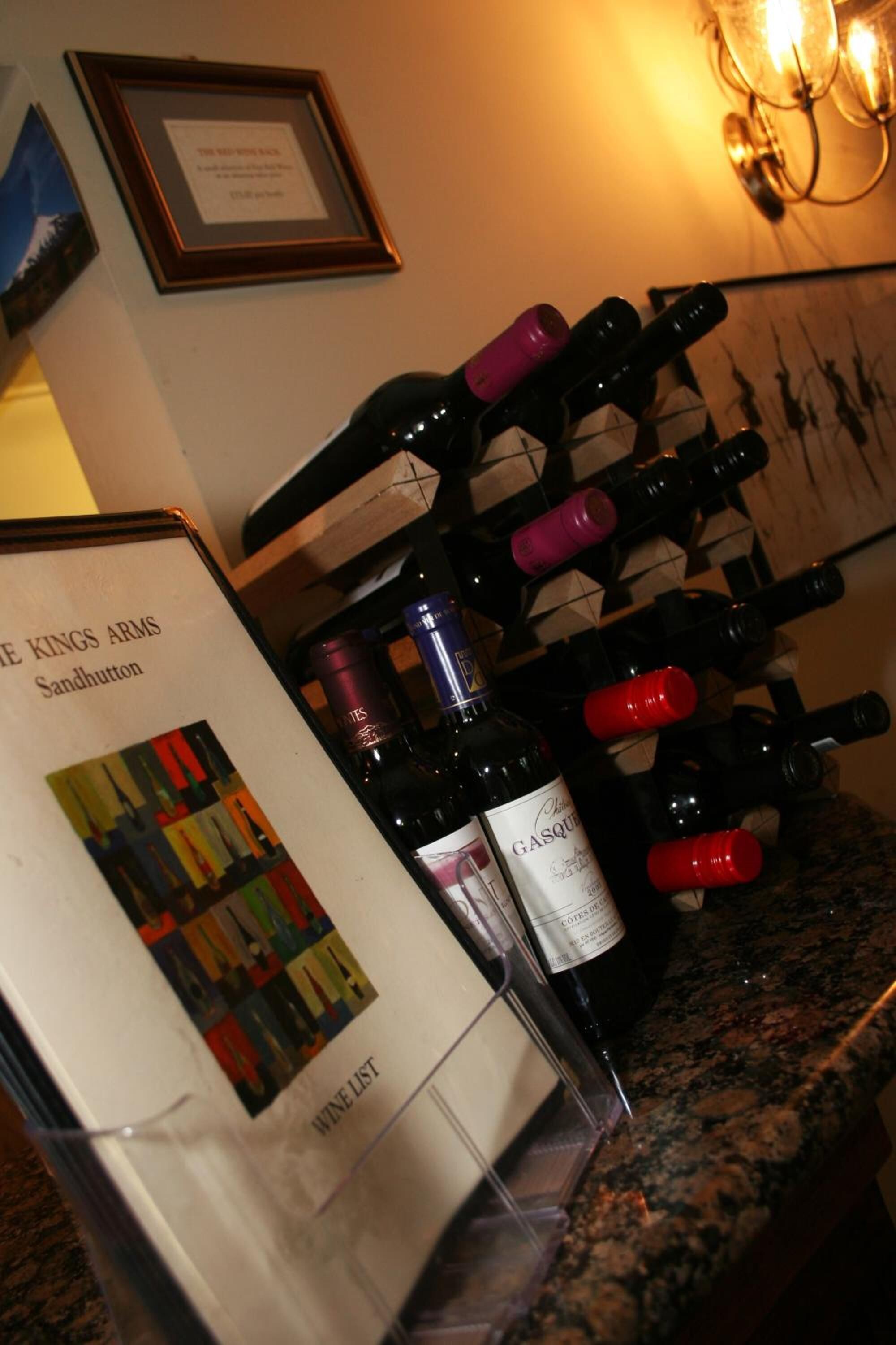 Ein Weinschränk mit verschiedenen Flaschen, ein gerahmtes Zertifikat an der Wand und eine Weinkarte auf der Theke.