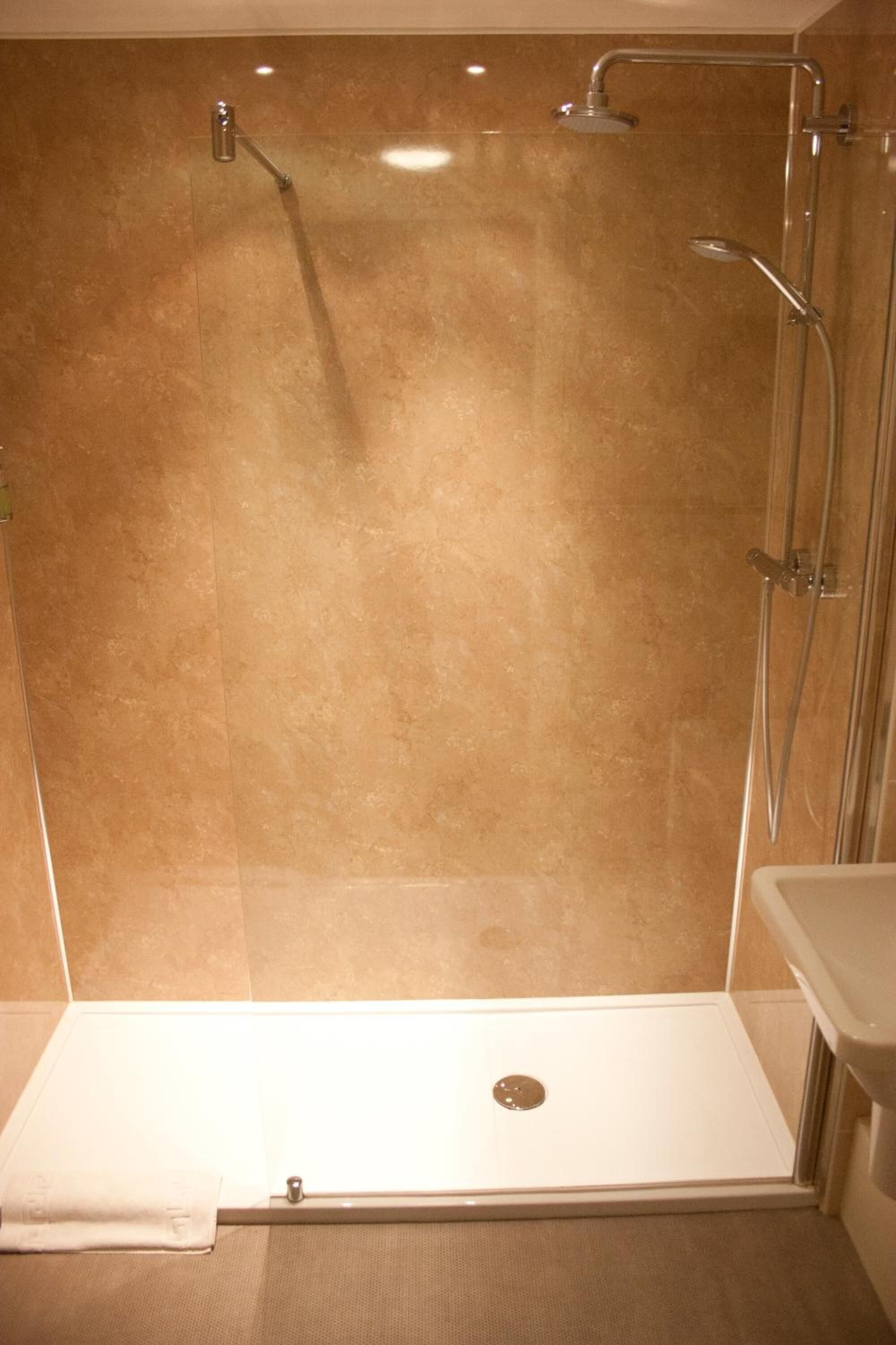 Una doccia a filo pavimento con porta in vetro, una vasca da bagno bianca e una parete rivestita di piastrelle color beige.