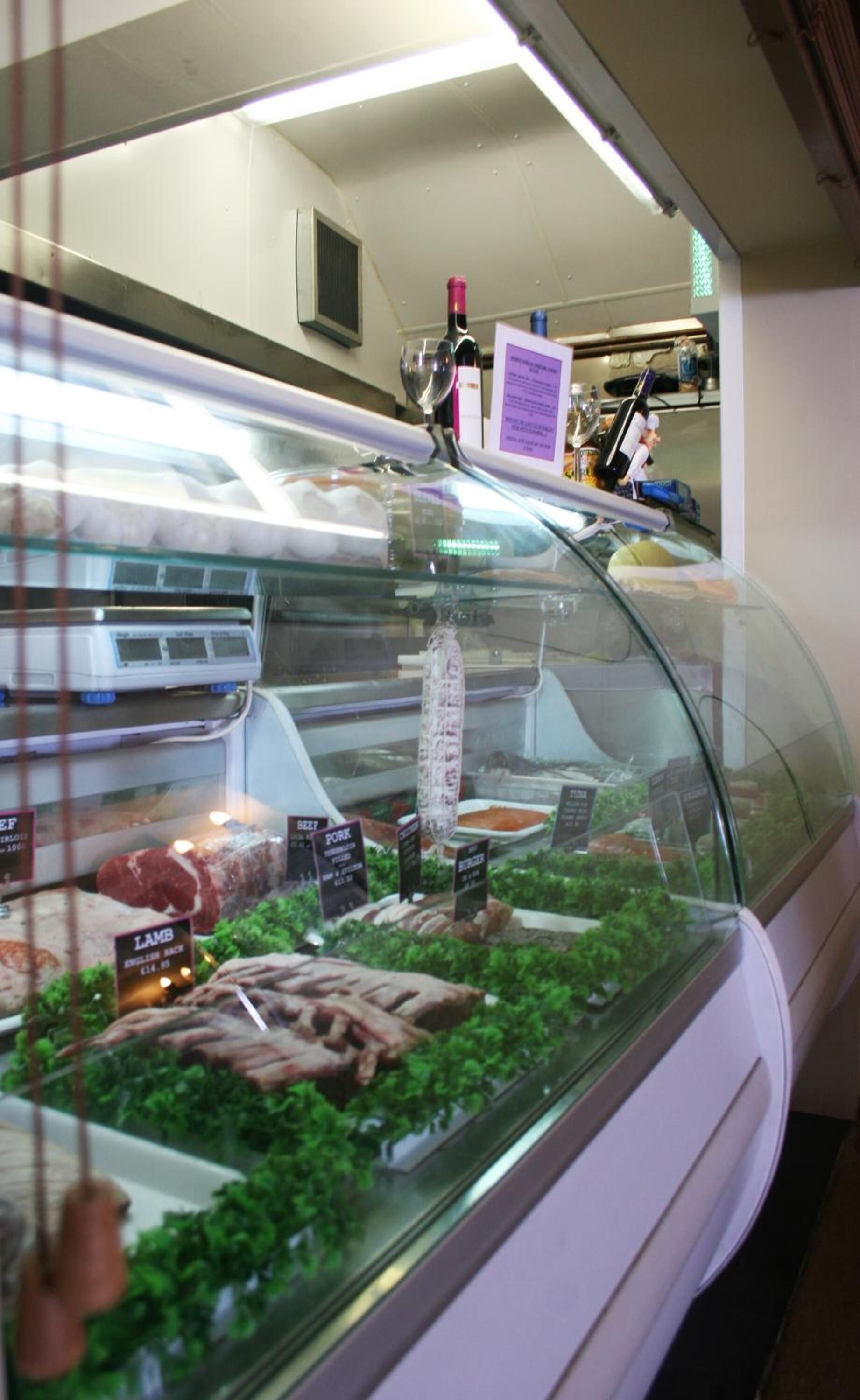 A deli counter with various meats displayed, including beef, pork, and lamb, with price tags visible.