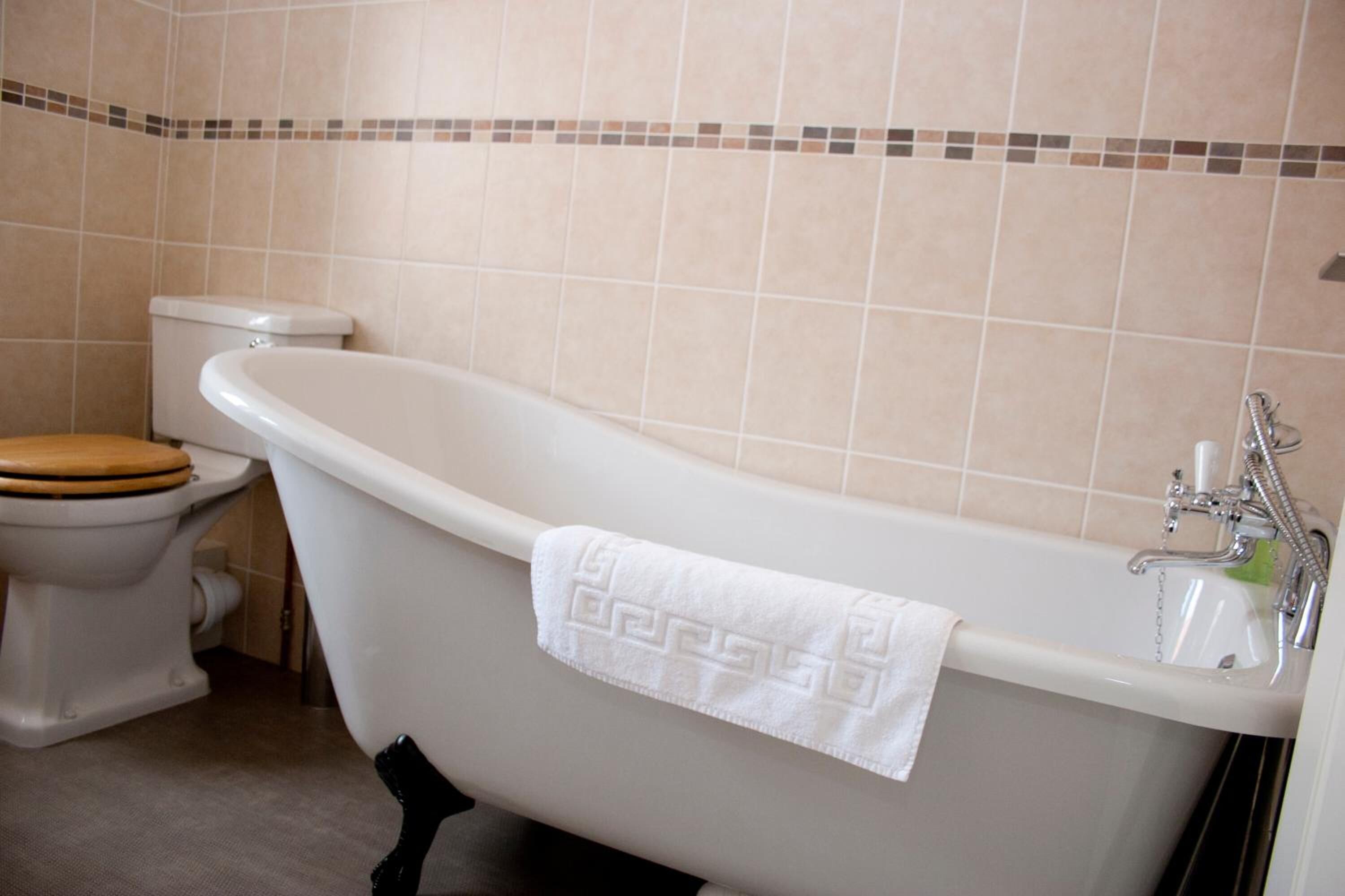 A bathroom with a freestanding bathtub, toilet, and a wooden toilet seat.
