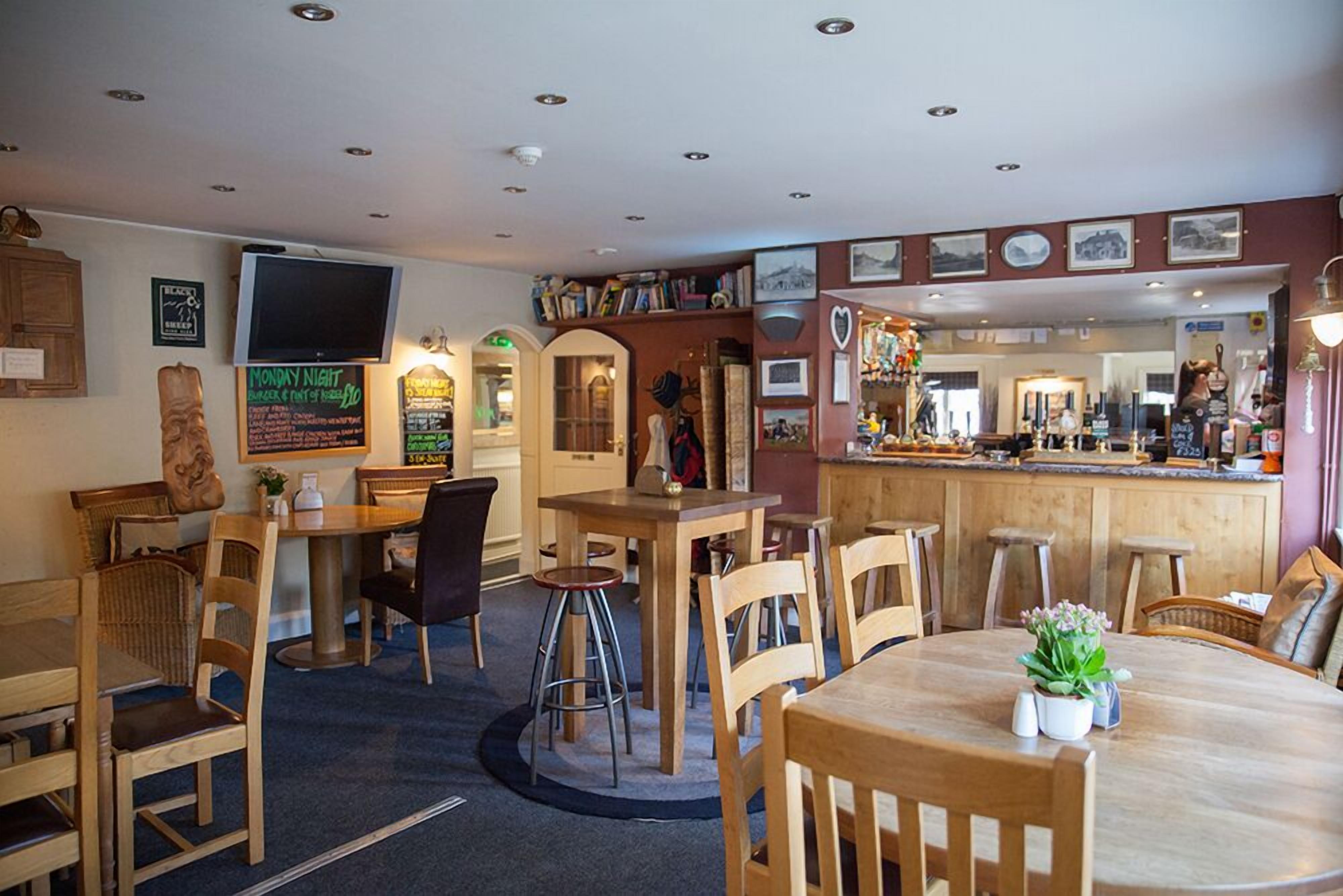 A cozy restaurant with wooden tables and chairs, a bar area, and various wall decorations including framed pictures and a chalkboard menu.
