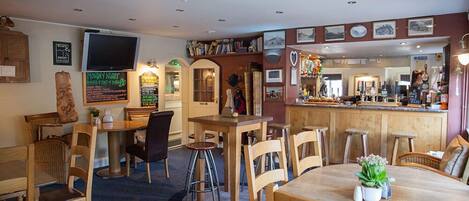 A cozy restaurant with wooden tables and chairs, a bar area, and various wall decorations including framed pictures and a chalkboard menu.