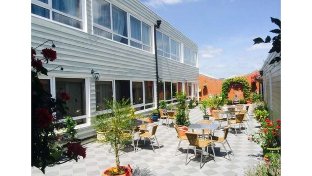An outdoor patio with tables and chairs, surrounded by potted plants and flowers. - The Globe Hotel (Colchester)
