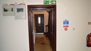 A hallway with a fire exit sign, a fire action sign, and a fire extinguisher on the wall. - The Globe Hotel (Colchester)