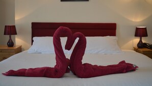 A bed with a red headboard, white pillows, and a red towel arrangement on the bed. - The Globe Hotel (Colchester)