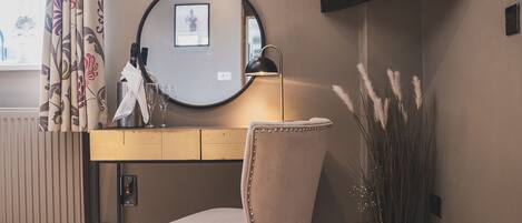 A room with a wooden desk, a chair, a round mirror, a television mounted on the wall, and a radiator.