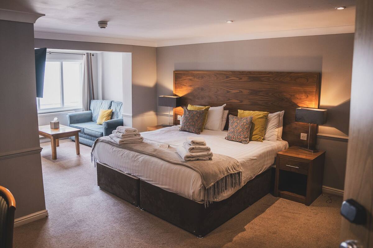 Una habitación de hotel con una cama grande, mesitas de noche, un sofá y una ventana.