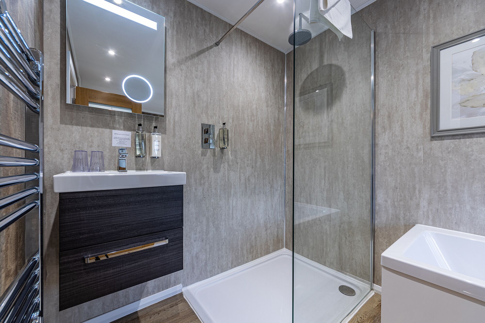A modern bathroom with a glass shower enclosure, a vanity with a dark wood drawer, and a large mirror with integrated lighting.