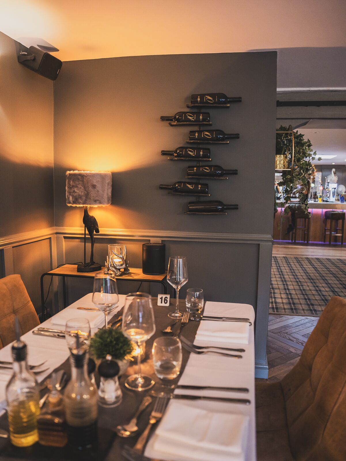 A restaurant setting with a table set for dining, a wall-mounted wine rack, and a bar area in the background.