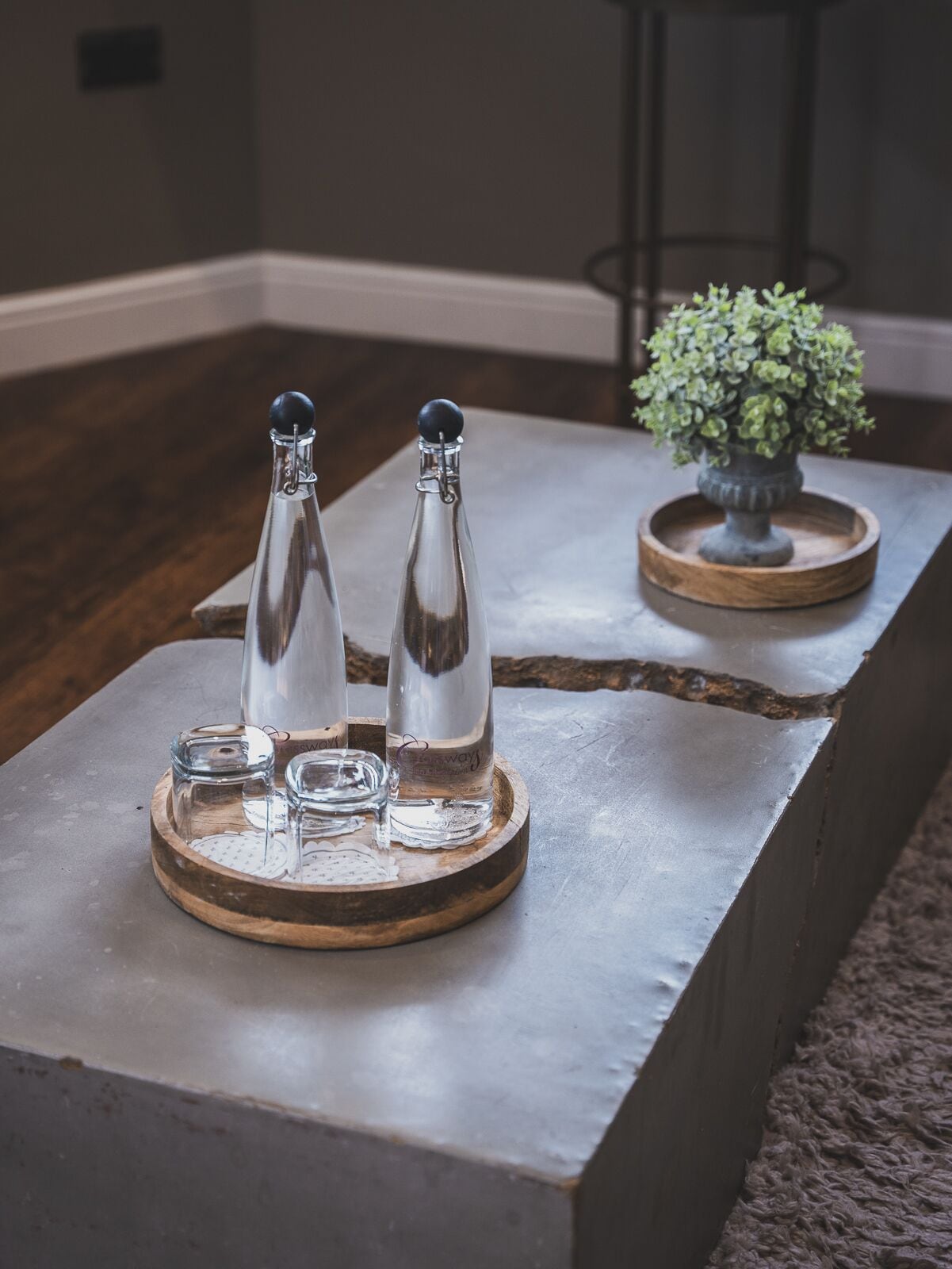 Un salon moderne avec une table basse en bois, agrémentée de deux bouteilles en verre et d’un sous-verre.