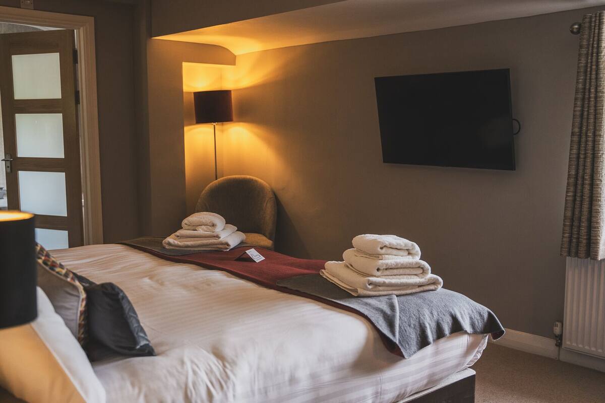 Una habitación de hotel con cama, una silla, televisión montada en la pared y una lámpara.