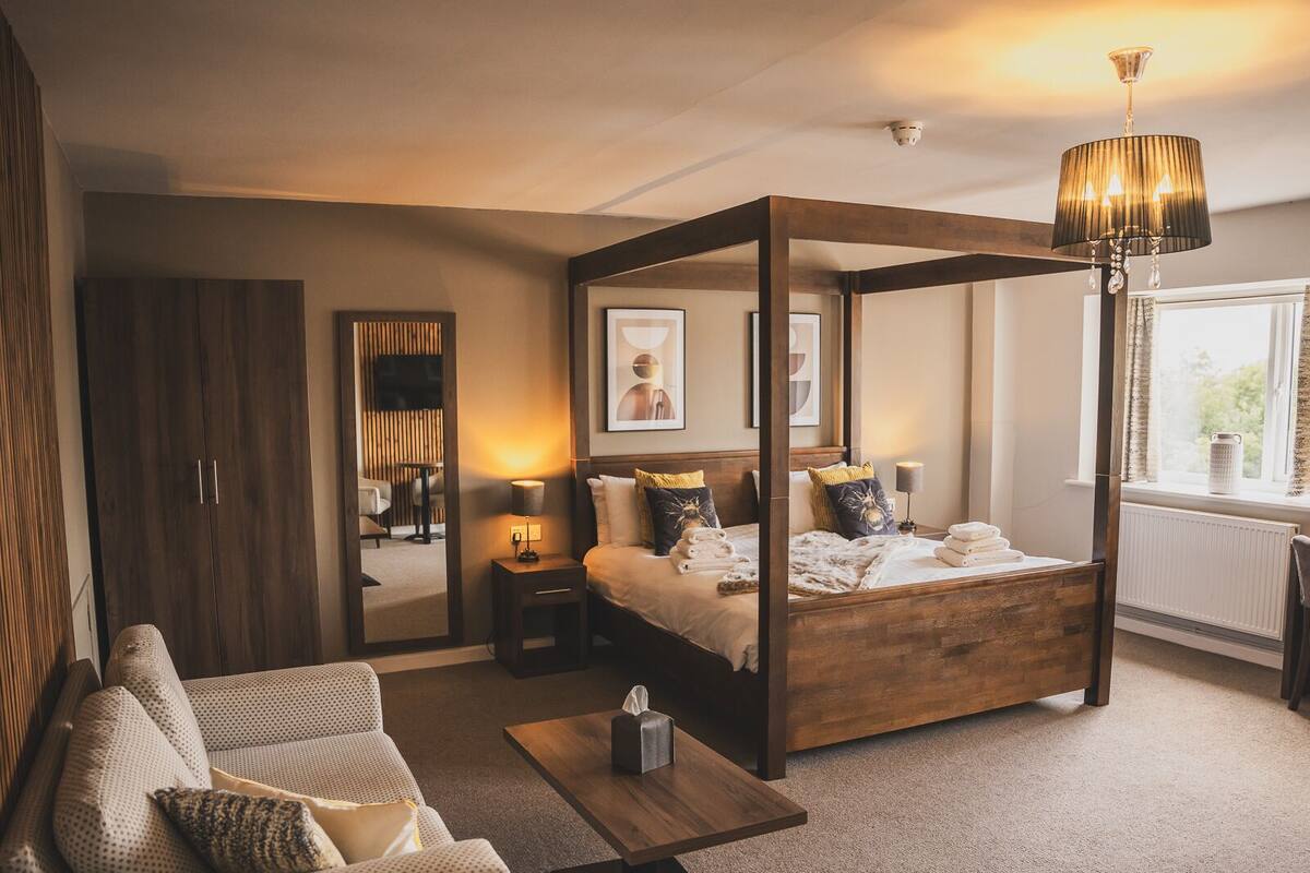 Un dormitorio moderno con cama con dosel, un espacio de descanso con sofá y mesa de centro, y un ventanal con vistas.