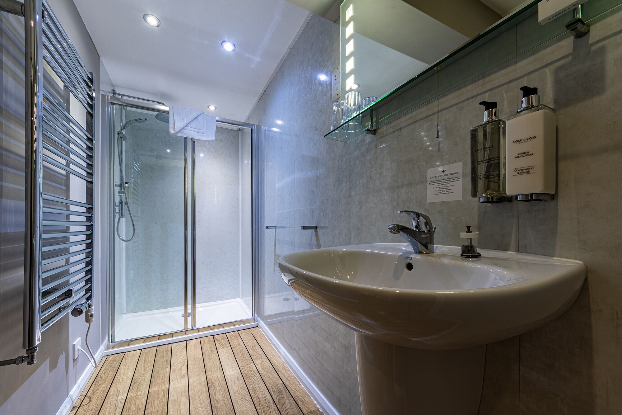 Ein modernes Badezimmer mit Duschkabine aus Glas, einem großen Waschbecken und Pflegeprodukten an der Wand.