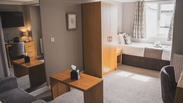 Habitación de hotel pequeña con cama, escritorio, armario y zona de estar.