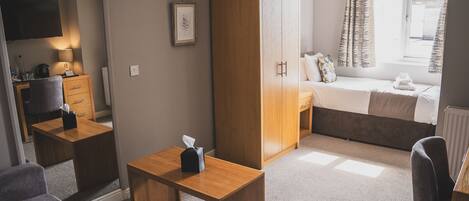 A compact hotel room with a bed, a desk, a wardrobe, and a seating area.