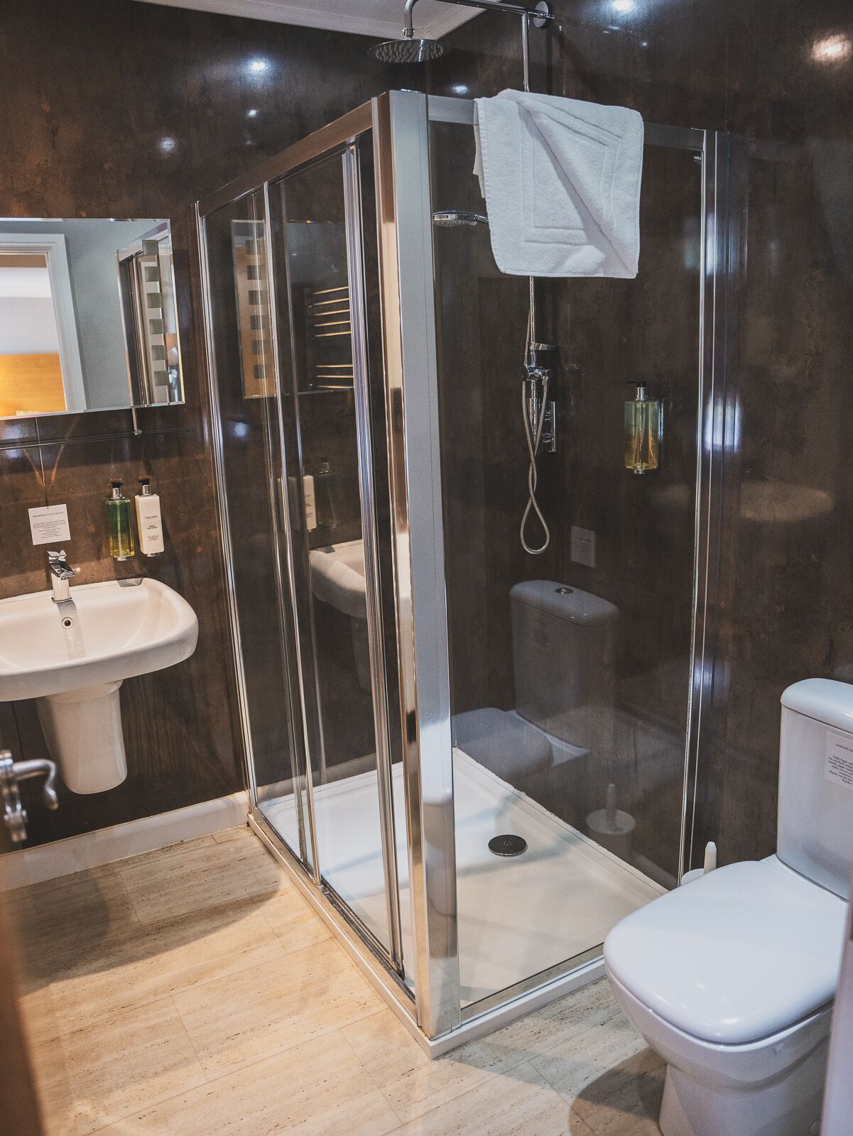 Un baño moderno con ducha de vidrio, un lavabo blanco y un inodoro.