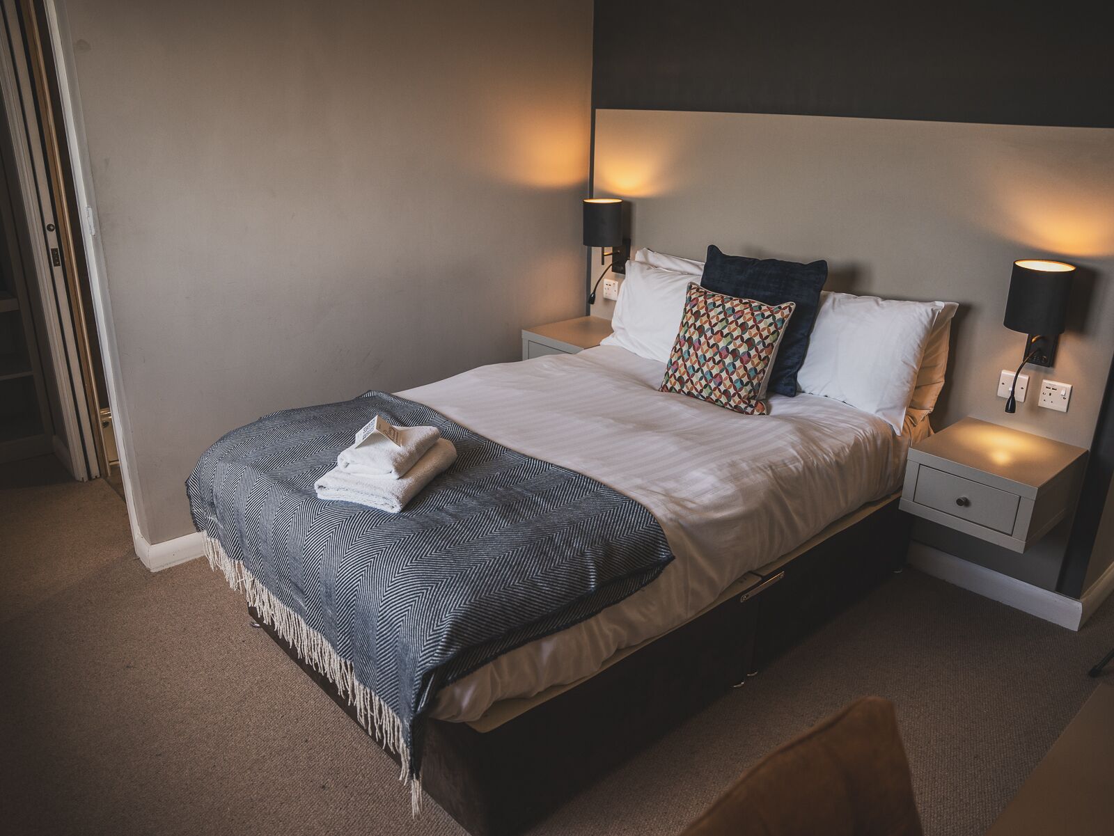 A neatly made bed with a patterned blanket, two pillows, and two bedside lamps.