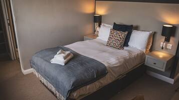 A neatly made bed with a patterned blanket, two pillows, and two bedside lamps.