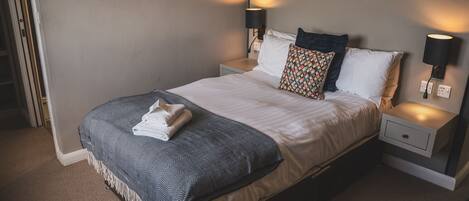 A neatly made bed with a patterned blanket, two pillows, and two bedside lamps.