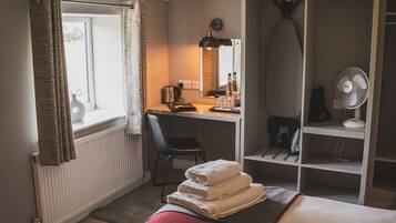 A hotel room with a bed, a desk with a chair, a wardrobe, a radiator, and a window with curtains.