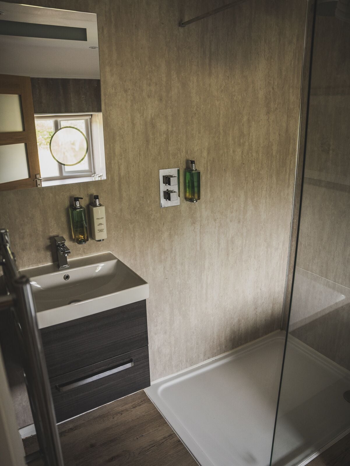 A modern bathroom with a glass shower enclosure, a sink with a dark cabinet, and toiletries on the wall.