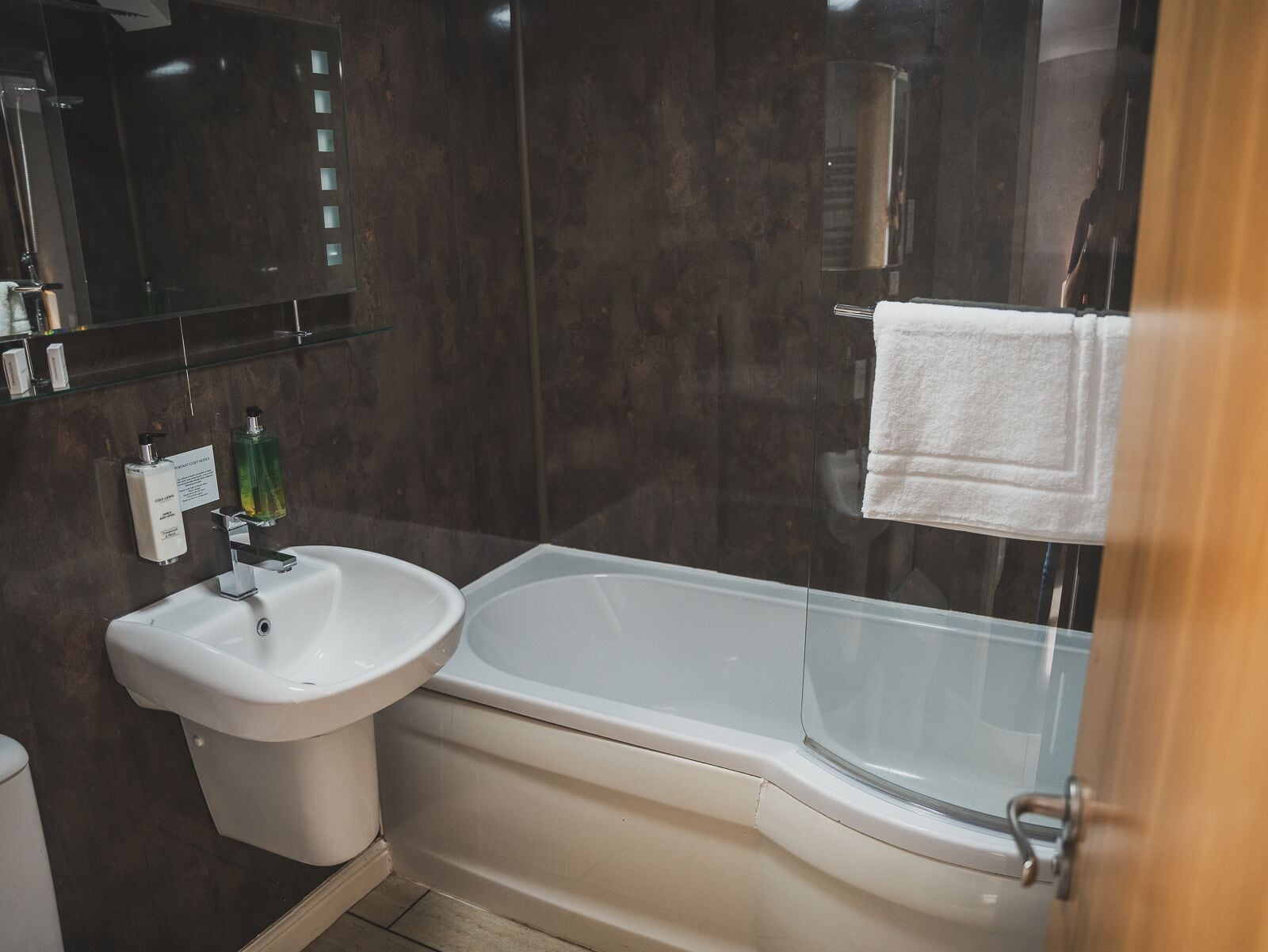A modern bathroom with a white sink, a glass-enclosed bathtub, and a mirror above the sink.