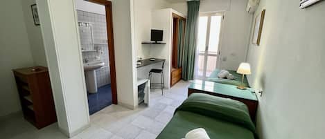 Ein Hotelzimmer mit Bett, Schreibtisch, Sessel, Waschbecken und Fernseher.
