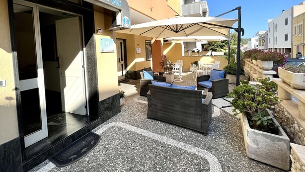 Hotelgevel met terras en zitplaatsen, een bord met de tekst 'Hotel Minerva' en een helderblauwe lucht.
