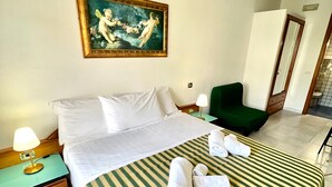Een hotelkamer met een bed, een groene fauteuil, een schilderij aan de muur en een badkamer die door een open deur zichtbaar is.