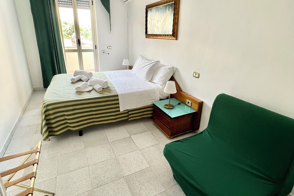 A hotel room with a bed, a green sofa, a small table, and a chair.