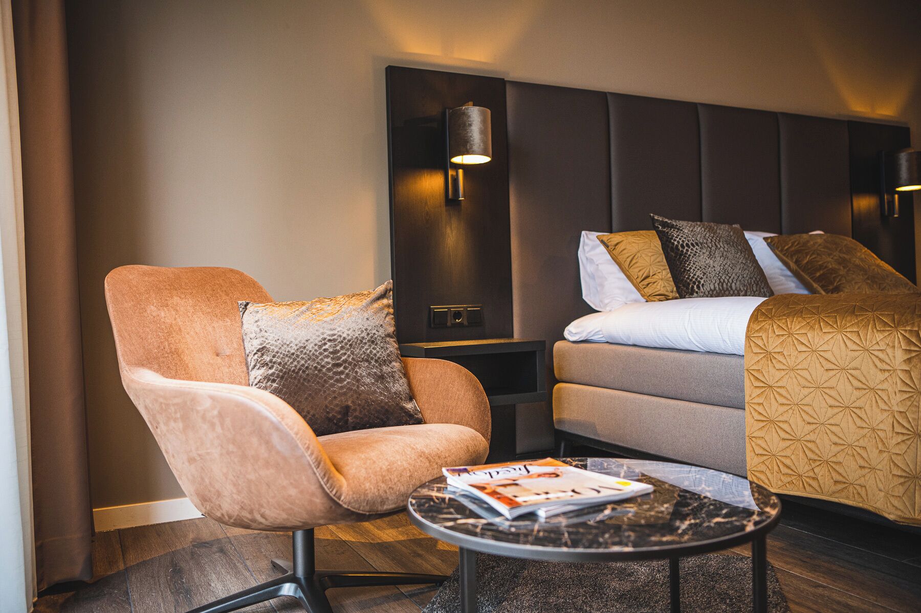 Een hotelkamer met een eenpersoonsbed, een slaapbank, een kleine tafel met een tijdschrift en een wandlamp.