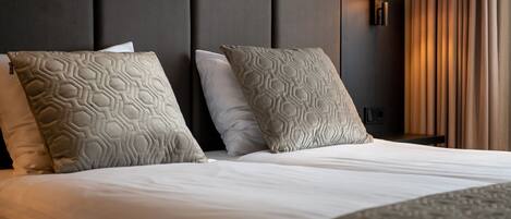 A hotel room with a large bed, two patterned pillows, a wall-mounted lamp, and a window with curtains.