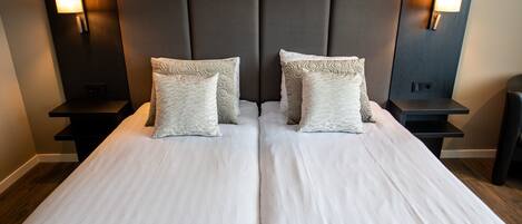 A double bed with a patterned bedspread, two pillows, and two bedside tables with wall-mounted lamps.