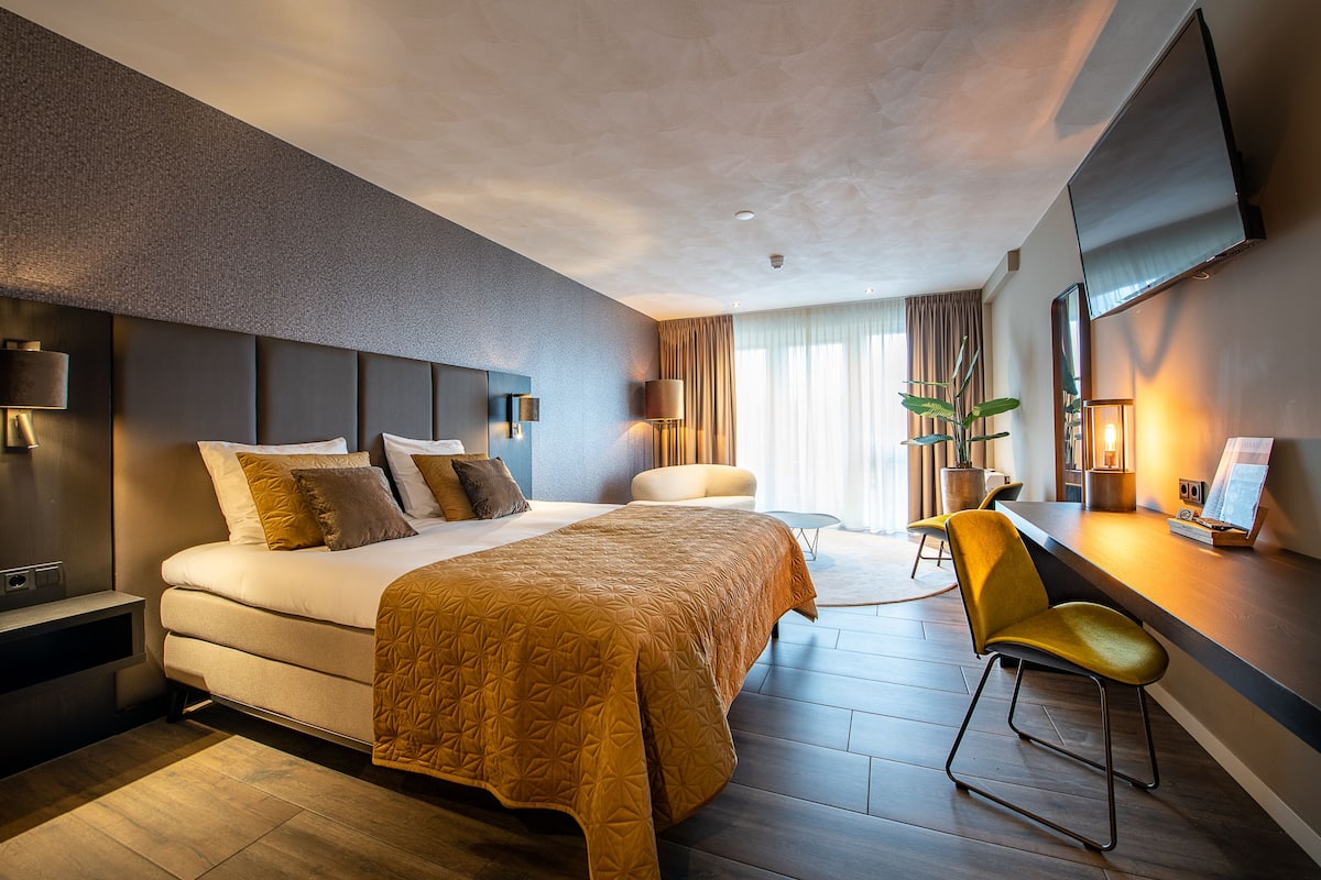 Une chambre d’hôtel moderne dotée d’un grand lit, d’un bureau avec une chaise, d’un téléviseur à écran plat et d’une grande fenêtre avec des rideaux.