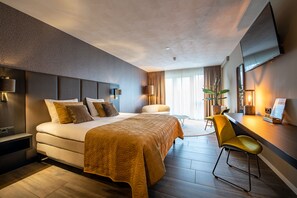 A modern hotel room with a large bed, a desk with a chair, a flat-screen TV, and a large window with curtains. - Maashof (Venlo)