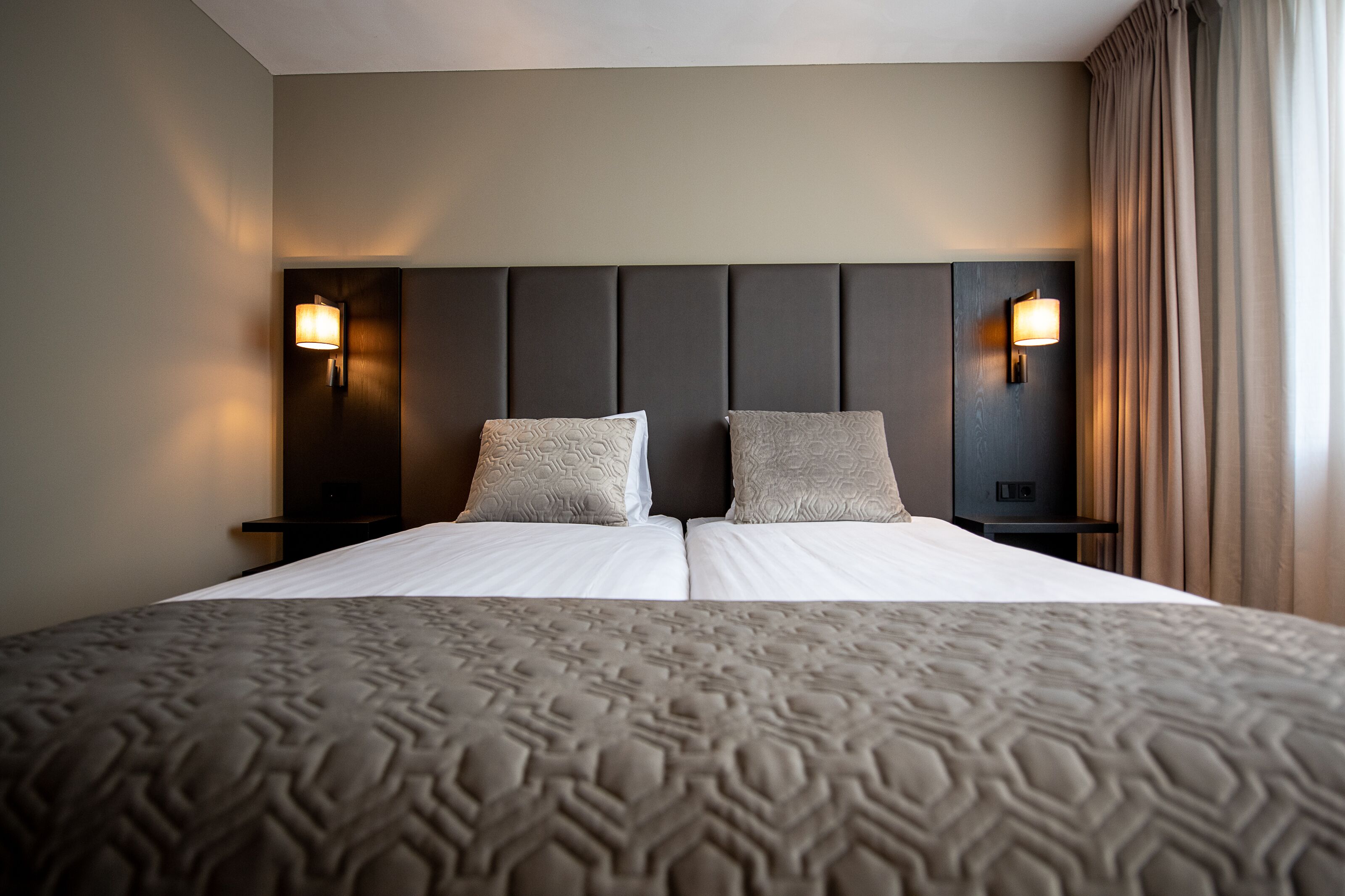 A double bed with a patterned bedspread, two pillows, and a headboard with wall-mounted lights.